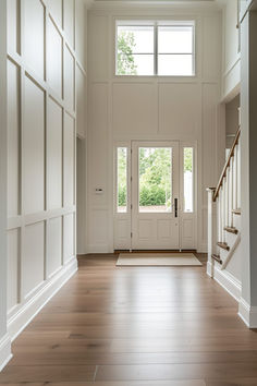 an empty entryway with wooden floors and white walls, leading to the front door