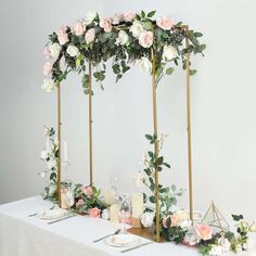 an arrangement of flowers and candles on a white table cloth with gold stand for the centerpieces