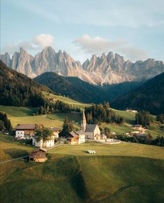 a small village in the middle of a green valley with mountains in the back ground