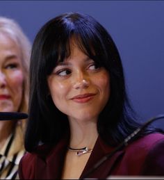 two women sitting next to each other in front of a microphone with one woman looking at the camera