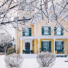 a yellow house with green shutters and snow on the ground in front of it