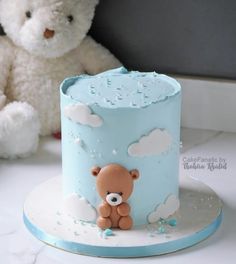 a teddy bear sitting next to a blue and white cake with clouds on the top