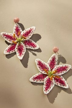 two pink and white flower shaped earrings on top of a beige surface next to each other