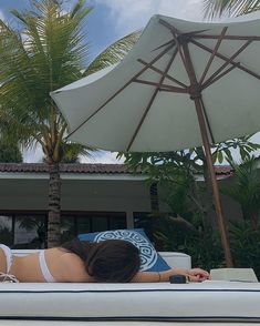 a woman laying on top of a white couch under an umbrella next to a palm tree