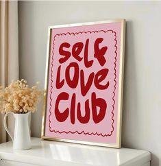 a pink poster with the words self love club on it next to a white vase