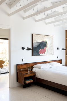 a bed sitting under a painting on the wall next to a desk with a lamp