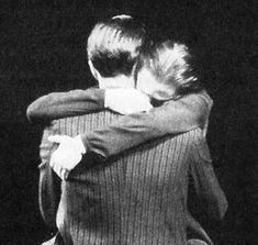 two people hugging each other in front of a black background