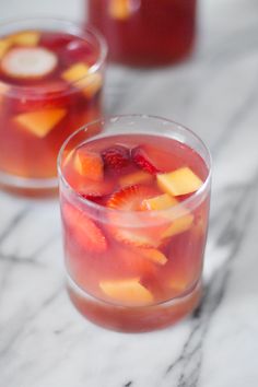 two glasses filled with fruit drink on top of a marble countertop next to each other