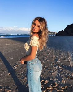 a woman standing on top of a sandy beach next to the ocean with her hair blowing in the wind