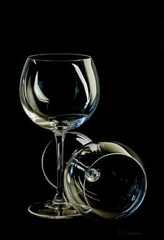 two wine glasses sitting next to each other on a black tableclothed surface, with one empty glass in the foreground