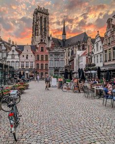 a cobblestone street with tables and chairs in front of an old church tower