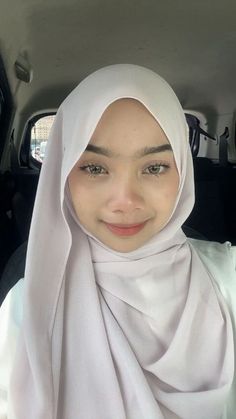 a young woman wearing a white hijab in the back of a car with her eyes wide open