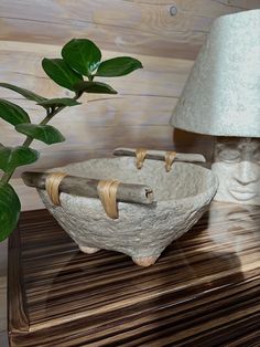 a wooden table topped with a white bowl next to a green plant and a lamp