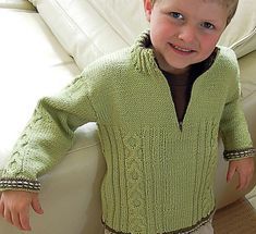 a little boy standing next to a couch wearing a green sweater