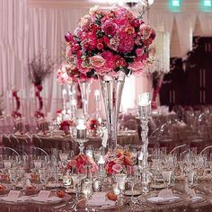 a tall vase filled with pink flowers sitting on top of a table covered in wine glasses