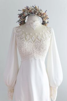 a white dress with long sleeves and flowers on the collar, is displayed in front of a