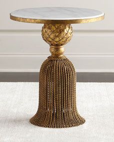 a gold table with a white marble top and tassels on the base, in front of a wall