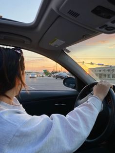 the woman is driving her car down the street at sunset or dawn, with cars in the background