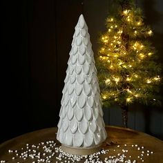 a white ceramic christmas tree sitting on top of a wooden table next to a pine tree