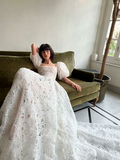 a woman in a white dress sitting on a green couch with her arms behind her head