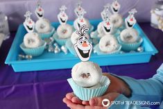 a person holding up a frosted cupcake in front of other cupcakes