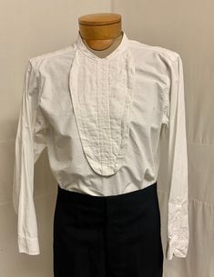 "1900, 15\" Neck, plain cotton boiled front bib shirt, collarless. Button in back half way. Long sleeves single French cuffs.  Curved at each hip at bottom.   Measurements: 15\" Neck 38\" chest Shoulder to shoulder  15\" Shoulder to hem  34\" Sleeves 23\" Arm holes 8\" Width at bottom. 42\" Condition excellent" Traditional Fitted Shirt With Buttons, Fitted Dress Shirt For Daywear, Traditional Cotton Workwear Tops, Classic Cotton Blouse With Covered Buttons, Classic Fitted Tops With Pintucks, Classic Daywear Tops With Pintucks, Vintage Shirt With Button Cuffs For Daywear, Traditional Long Sleeve Shirt For Daywear, French Cuff