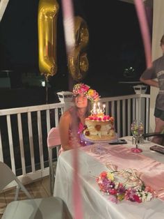 a woman sitting at a table with a cake on it and balloons in the air