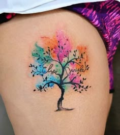 a colorful tree tattoo on the back of a woman's thigh, with words written in cursive writing