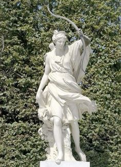 a white statue holding a staff in front of some trees