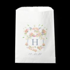 a white paper bag with the letter h on it and flowers in front of it