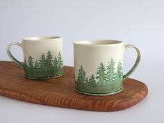 two green and white mugs sitting on top of a wooden board next to each other