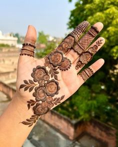 a woman's hand with henna tattoos on it and trees in the background