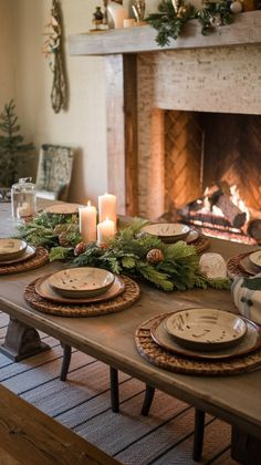 a table with plates and candles on it in front of a fireplace decorated for christmas