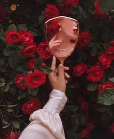 a woman's hand holding up a mirror in front of red roses