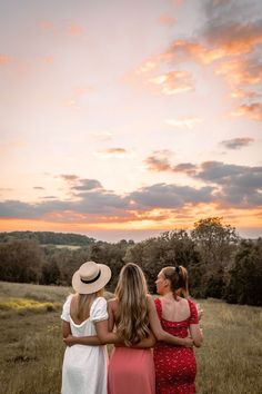 three women standing in a field at sunset with their arms around each other and looking up into the sky