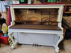 an old piano sitting in a garage with lots of other items on the floor behind it