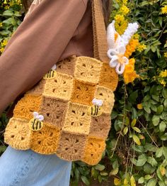 a woman carrying a crocheted bag with bees on it and flowers in the background