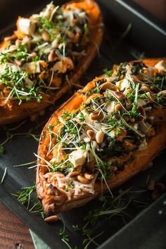 two baked sweet potatoes topped with greens and nuts