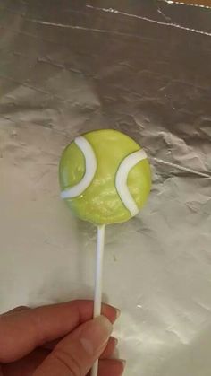 a hand holding a lollipop with a tennis ball on it