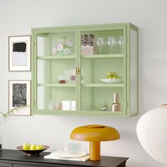 a green cabinet with glass doors and shelves on the wall next to a black dresser