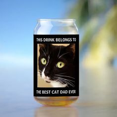 a black and white cat with green eyes in a jar that says, this drink belongs to the best cat dad ever