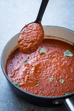 a ladle full of red sauce being held by a spoon