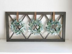 three wreaths are hanging on the wall above a shelf with clothes pins attached to them