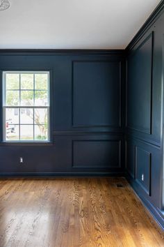 an empty room with dark blue walls and wood floors