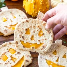 a person holding a piece of bread with carved pumpkin faces on it and other food items in the background