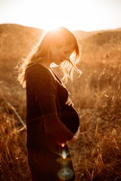 a pregnant woman standing in tall grass with the sun shining down on her belly and back