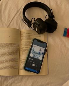 an open book with headphones on top of it next to a cell phone and earbuds