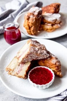 two white plates topped with pastries covered in powdered sugar next to a cup of jelly