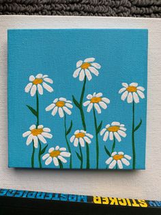 Painting on a square canvas. Light blue background. 10 daisies are painted, with yellow middles and white petals. Their dark green stems come up from the bottom of the canvas, and they each have one leaf. What To Draw With Acrylic Paint Easy, Painting On Blue Background, Blue Paintings On Canvas Easy, Painting Ideas With Blue Background, Blue Background Painting Easy, Acrylic Painting Blue Background, Simple Blue Painting Ideas, Simple Blue Paintings, Blue Easy Paintings