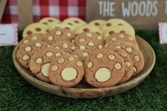 a wooden plate filled with cookies on top of a green grass covered field next to a red and white checkered tablecloth